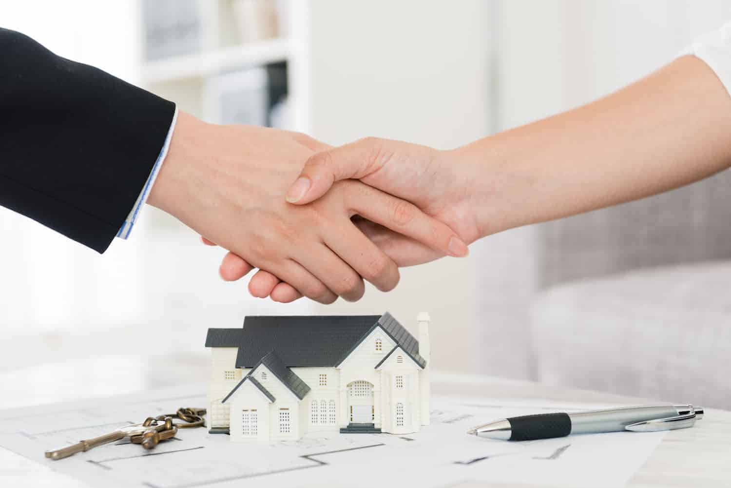 Mortgage lender and borrower shaking hands over plans of a home
