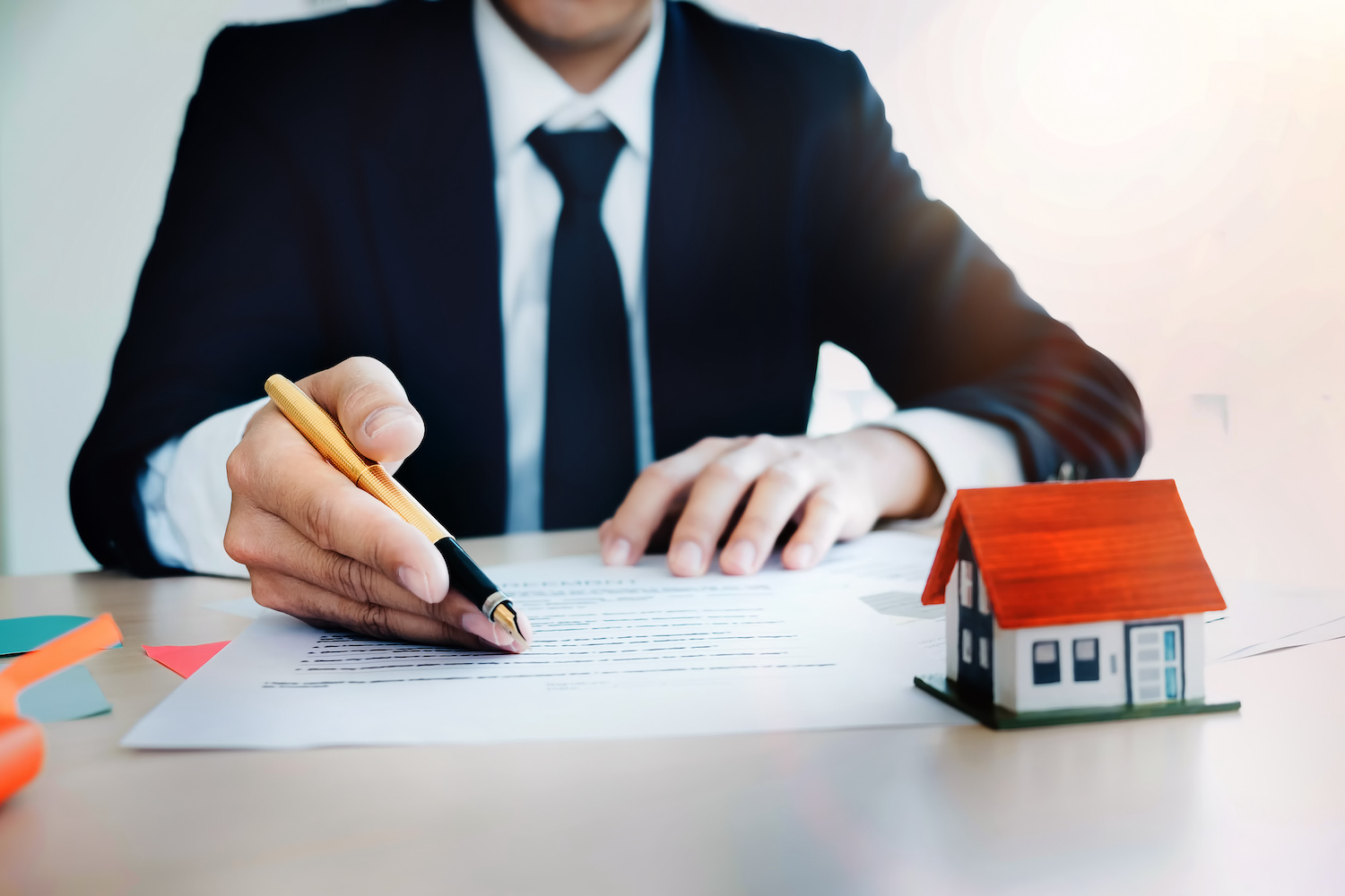 Person in suit inspecting paperwork for loan underwriting process. There is a small house model in front of them.