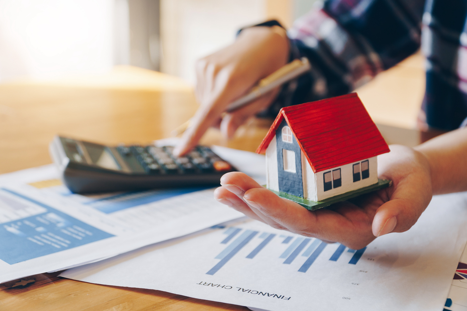 renovate-or-move Person holding small house model and crunching numbers on a calculator.