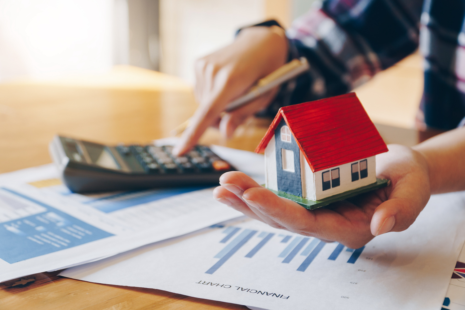 Person holding small house model and crunching numbers on a calculator. 