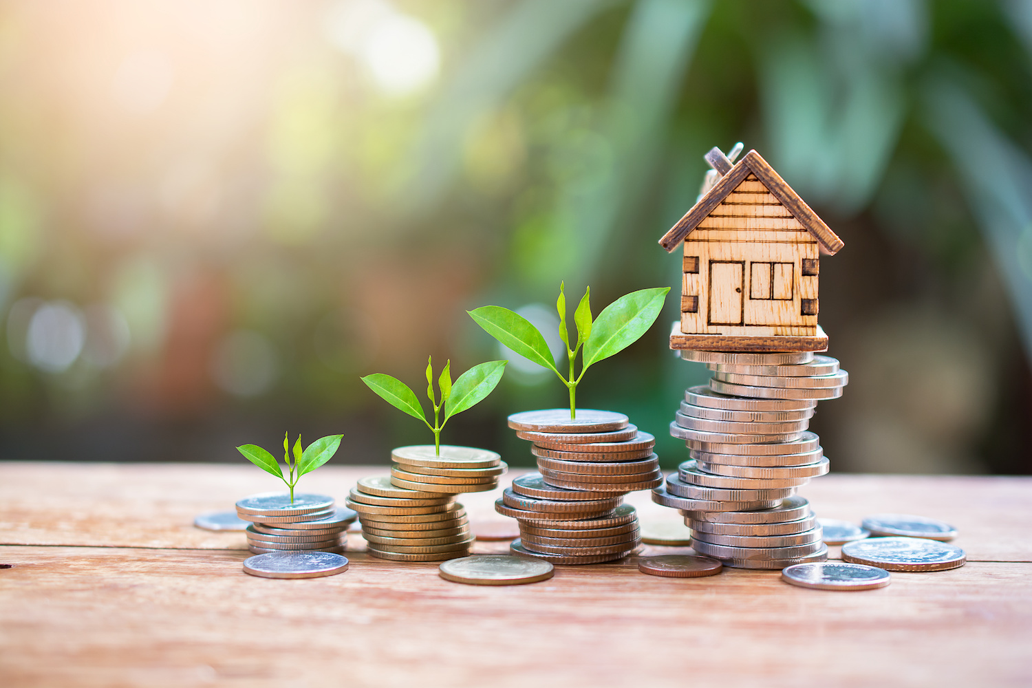 Stacks of coins with sprouts and a small house model sitting on top. 