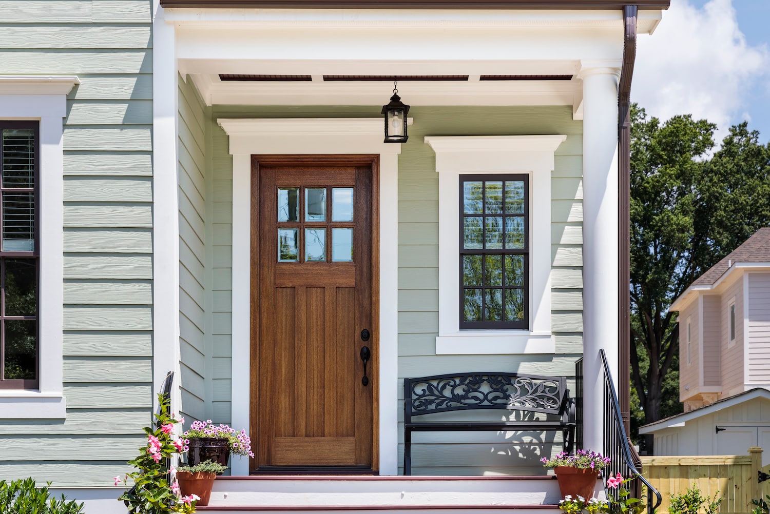 Front porch with brown door and wrought iron bench.